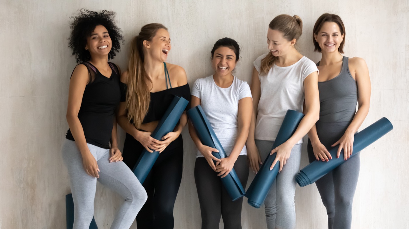 Smiling group of women holding yoga mats before class
