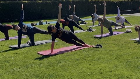 Outdoor mat Pilates class holding side plank on the lawn at Laurelwood Park, San Mateo